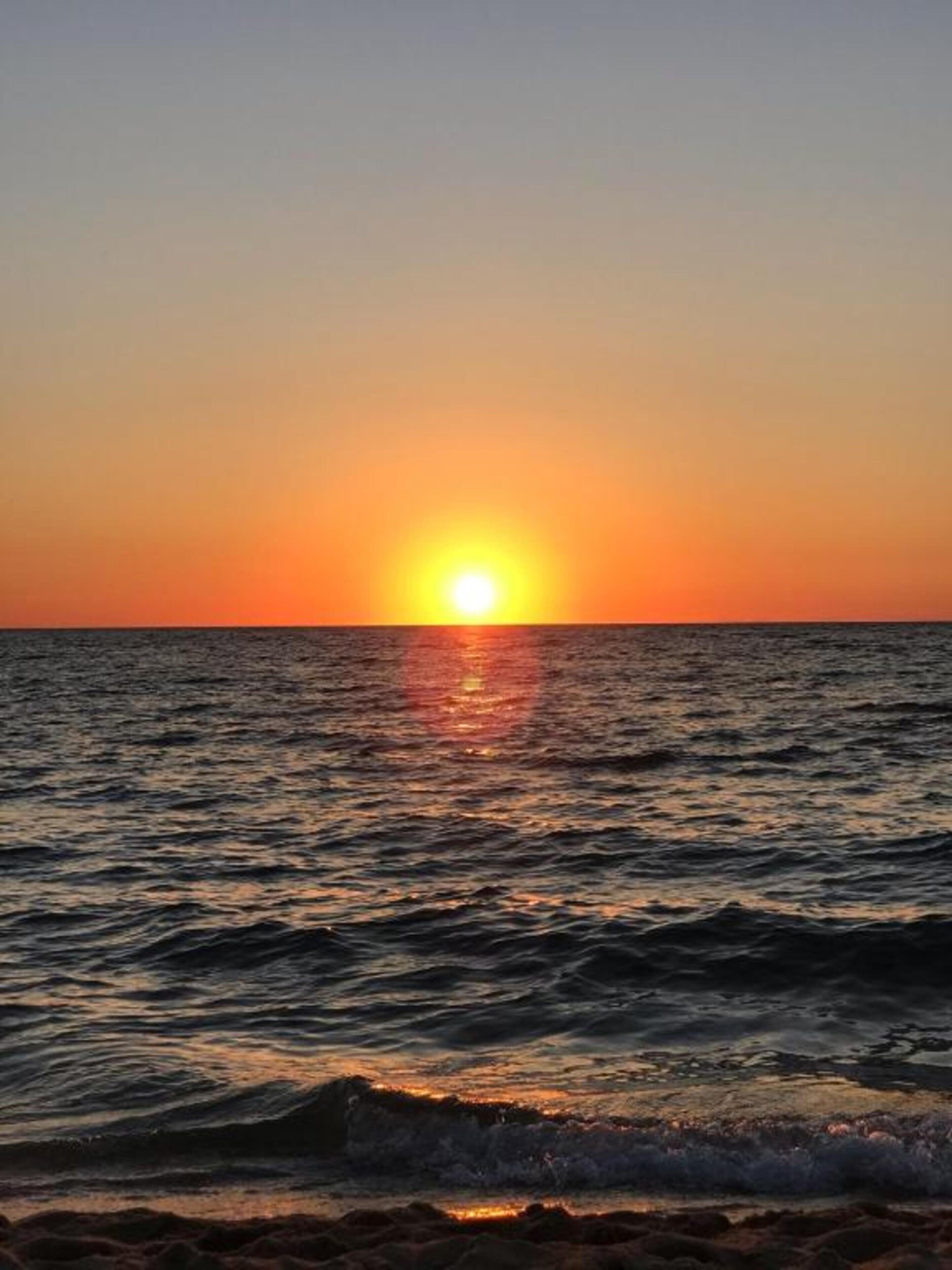 Un coucher de soleil sur l’océan, avec des vagues.
