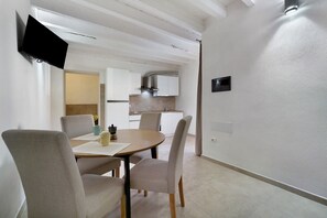 Un intérieur moderne comprenant un coin repas avec une table ronde et quatre chaises, une cuisine avec des meubles blancs et une hotte en acier inoxydable, et un mur à texture.