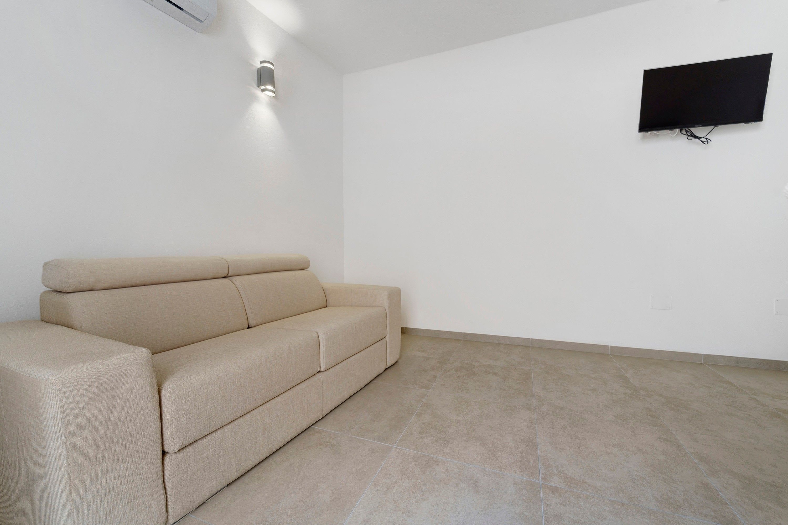 Een minimalistische woonkamer met een beige bank, een flatscreentelevisie aan de muur en een moderne airconditioning.