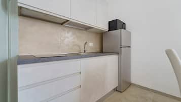Eine kompakte Küche mit integriertem Spülbecken, einem Edelstahl-Kühlschrank und einem einzelnen Schrank.