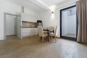 Een knus woongedeelte met een kitchenette, een eethoek met tafel en stoelen, en een schuifpui naar een balkon.
