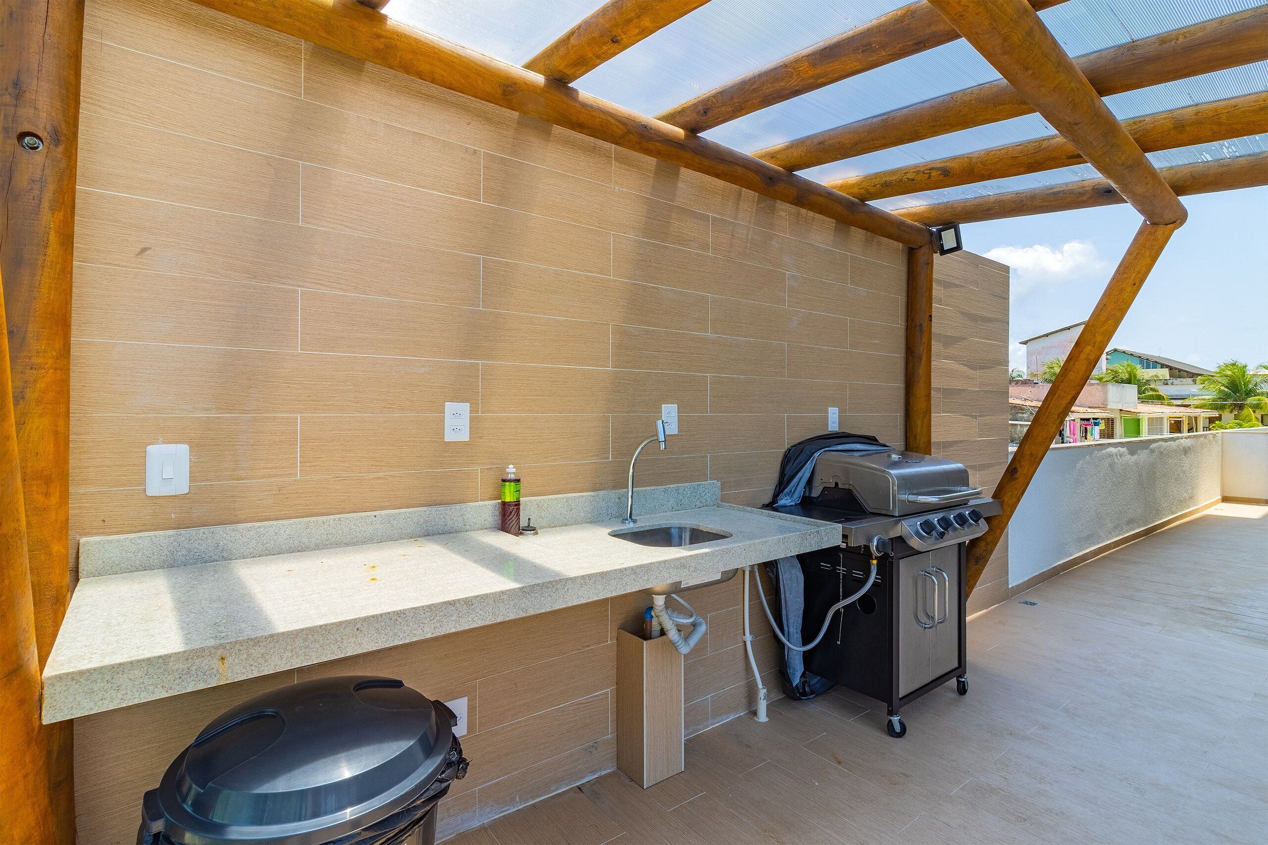 An outdoor kitchen with a sink, a grill, and a trash bin.