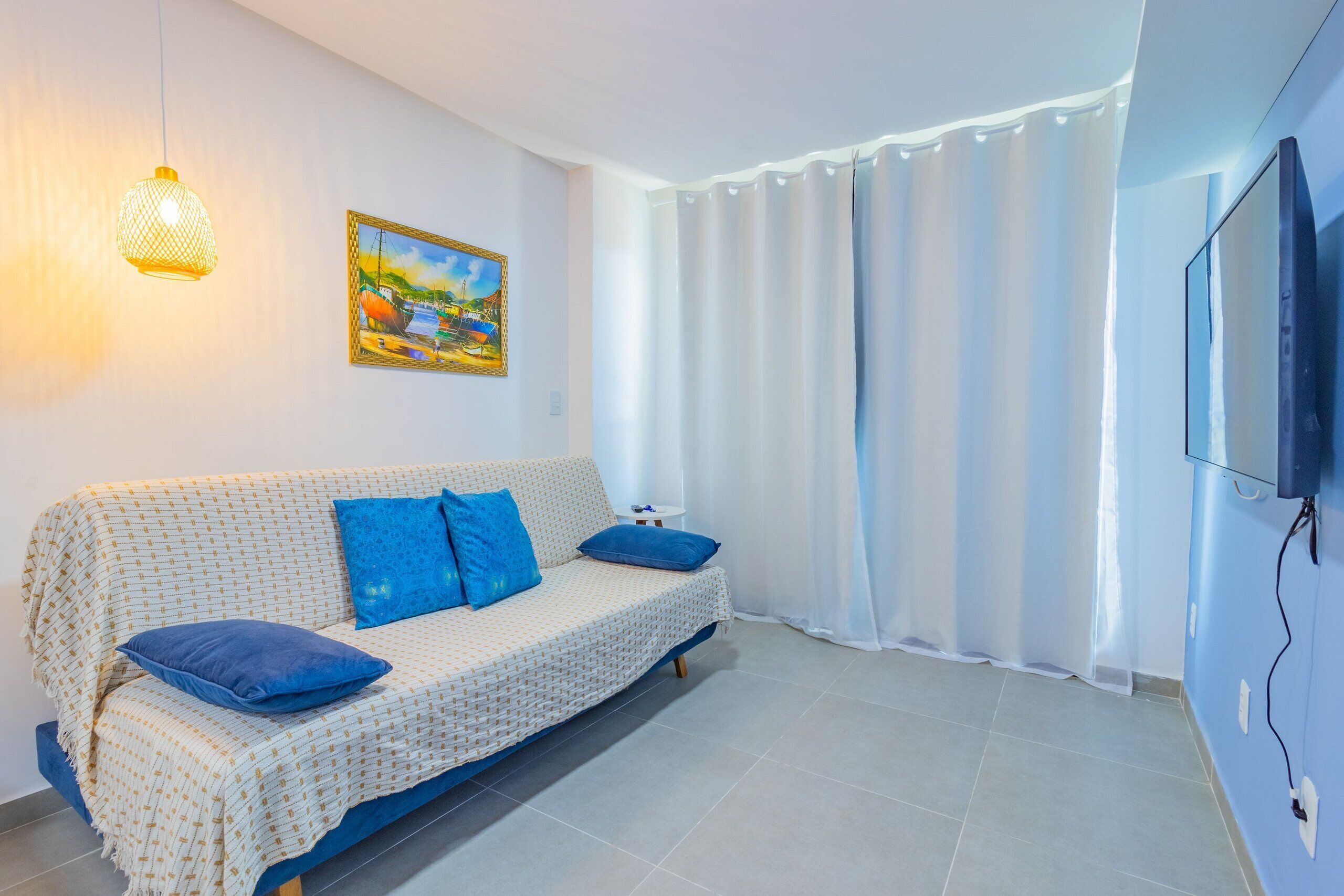 A living room with a sofa, blue cushions, a painting, a TV, and a curtain.