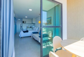 A hotel room with a bed, a small kitchenette, and a balcony with a table and chairs. - Villa Del Mar #206 - Quadruple by Carpediem (Ipojuca)
