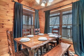 A wooden dining table set with plates and chairs, large windows with blinds, and a ceiling fan. - 🦌 The Mellow Moose | Hot Tub, Mountain Views & Game Loft, Near Dollywood (Pigeon Forge)