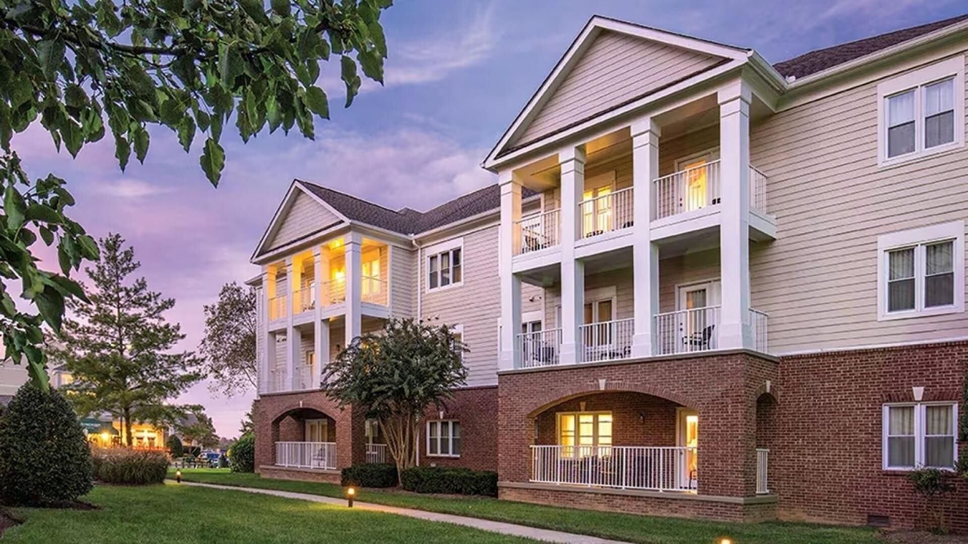 A multi-story residential building with a brick facade, multiple balconies, and a well-maintained lawn.