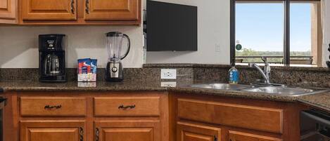 A kitchen with wooden cabinets, a coffee maker, a blender, and a sink.