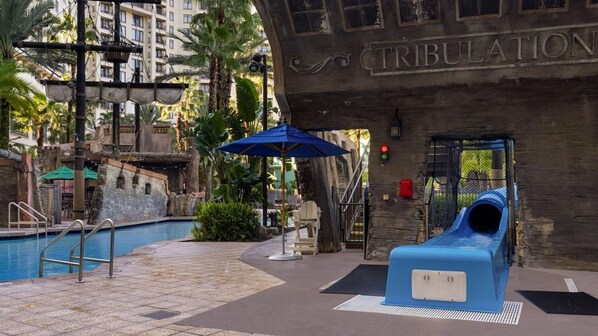 A pool area with a slide, a blue umbrella, and a sign that reads "TRIBULATION". - Near disney springs- 3 bdrm sleep 10 (Lake Buena Vista)