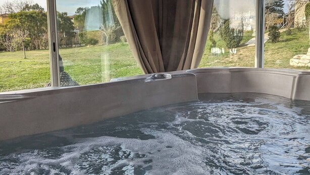 Un jacuzzi con vista a un área verde y árboles a través de amplias ventanas.