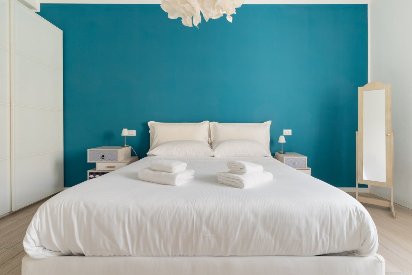 A large bed with white linens, two bedside tables with lamps, and a mirror on the wall.