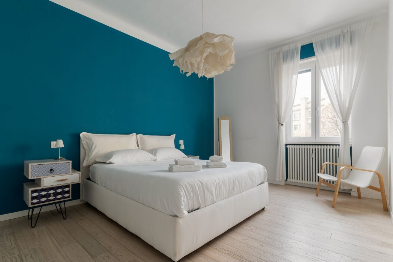 A bedroom with a bed, bedside table, lamp, chair, and a window with curtains.