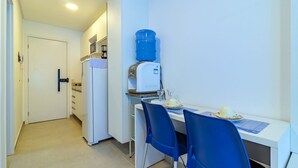 Una cocina compacta con dispensador de agua, un refrigerador y un comedor con dos sillas azules.