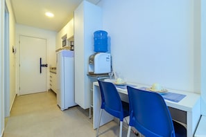 Eine kompakte Küche mit Wasserspender, einem Kühlschrank und einem Essbereich mit zwei blauen Stühlen.