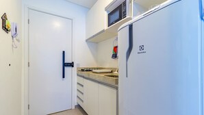 Una cocina compacta con armarios blancos, un microondas y un refrigerador.