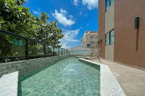 Ein Schwimmbecken mit klarem Wasser, umgeben von einer gefliesten Terrasse und einer Glasbrüstung.