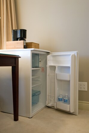 Un petit réfrigérateur doté d’un distributeur d ’eau, avec une machine à café posée sur le dessus et une petite boîte en bois fixée à la porte.