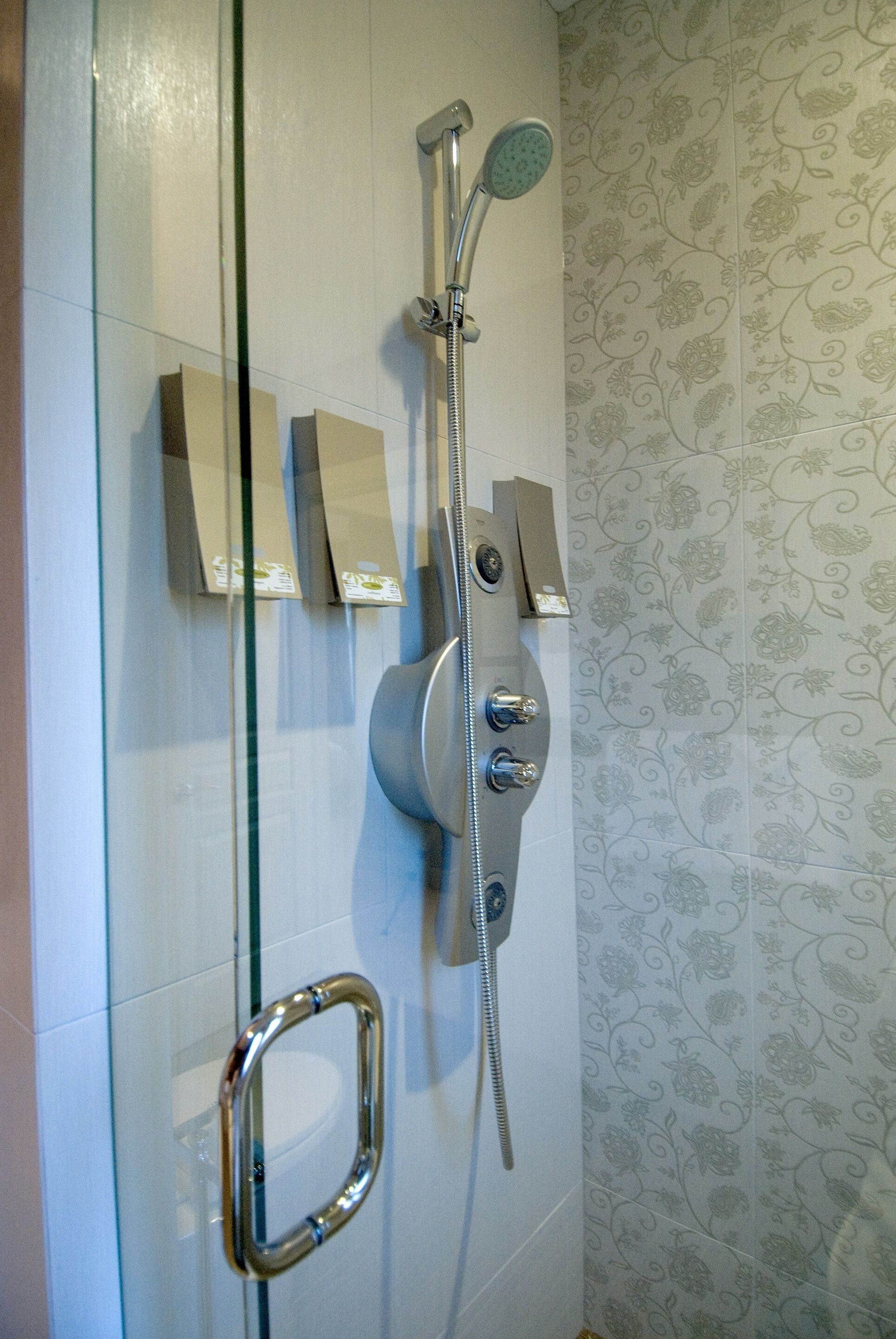 Ducha con cabezal de ducha de mano y cabezal fijo, instalada en una pared con estampado floral.