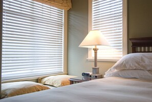 A hotel room with a bed, a bedside table with a lamp, and a window with blinds. - King bed, ensuite bathroom with shower (Vancouver)