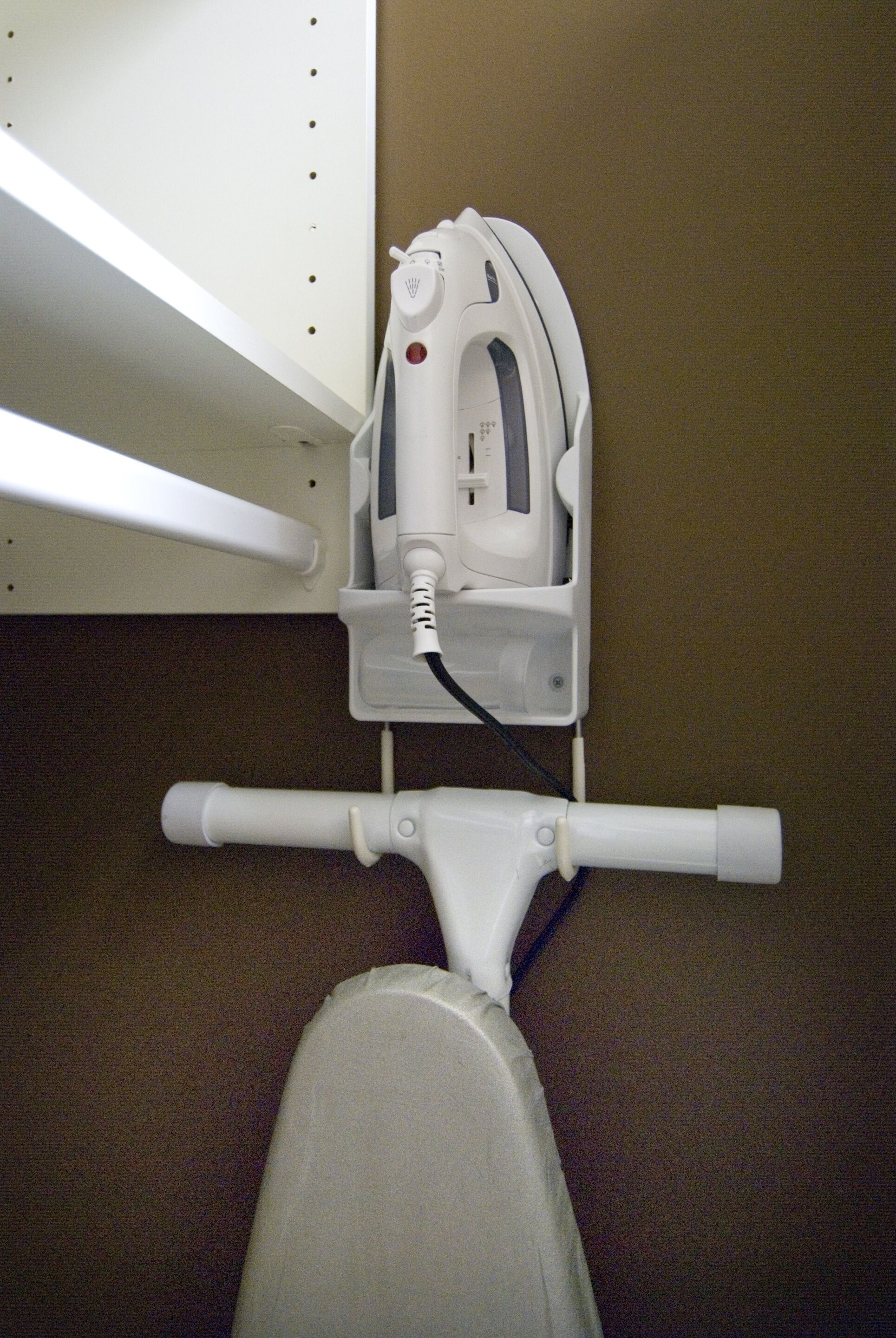 A white iron appliance mounted on a wall, a white ironing board, and a white chair.