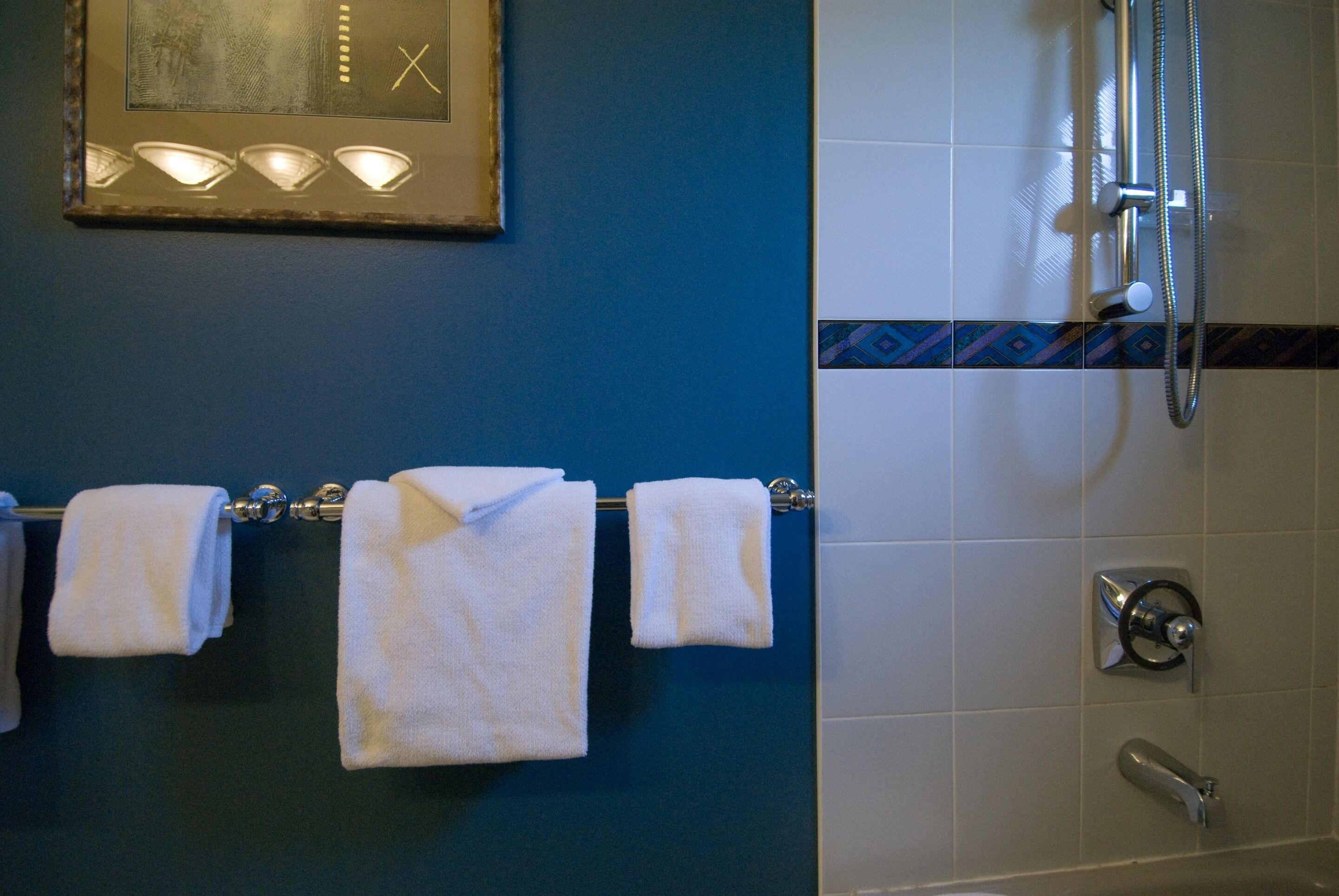Casa de banho com parede azul, zona de chuveiro com azulejos brancos e três toalhas brancas penduradas num suporte.