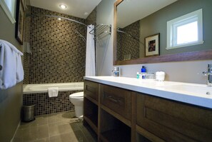 A bathroom with a bathtub, toilet, and a large mirror above the sink.