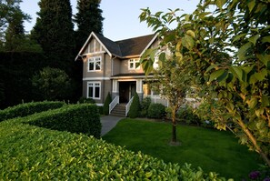 A two-story house with a front porch, a well-maintained lawn, and a small tree in the foreground.