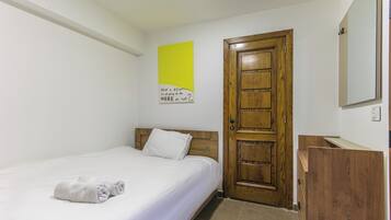 A hotel room with a single bed, a wooden door, a small wooden cabinet, and a wall-mounted mirror.
