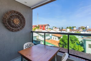 Ein Balkon mit Blick auf eine Wohngegend, einem Holztisch, einem weißen Stuhl und einer Wanddekoration.