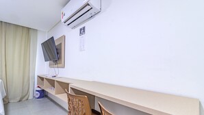 A hotel room with a long desk, two chairs, a flat-screen TV mounted on the wall, and an air conditioning unit above the desk. - Villa Del Mar #203- Flat With Balcony by Carpediem (Ipojuca)