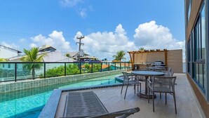 A rooftop pool area with a view of buildings and palm trees, a barbecue grill, and outdoor seating. - Villa Del Mar #203- Flat With Balcony by Carpediem (Ipojuca)