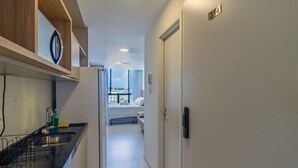 A narrow hallway with a kitchen area on the left, a bed with a view in the center, and a door with a number on the right. - Porto City #314 - Porto de Galinhas by Carpediem (Ipojuca)