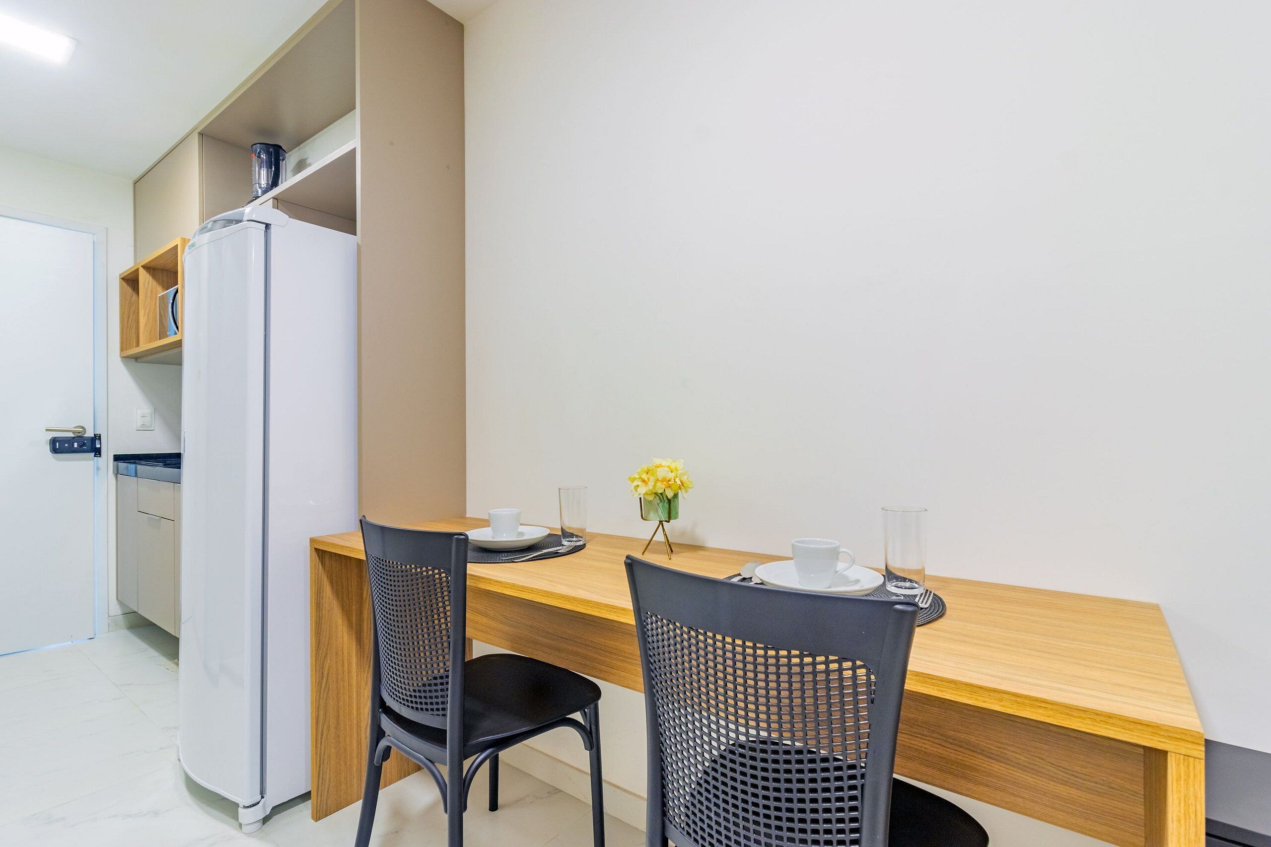A compact kitchen with a refrigerator, wooden cabinets, and a dining area with two chairs and a table.