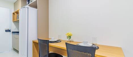 A compact kitchen with a refrigerator, wooden cabinets, and a dining area with two chairs and a table.