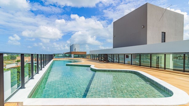 A modern swimming pool with a wooden deck, surrounded by glass railings and a clear sky. - Porto City #314 - Porto de Galinhas by Carpediem (Ipojuca)