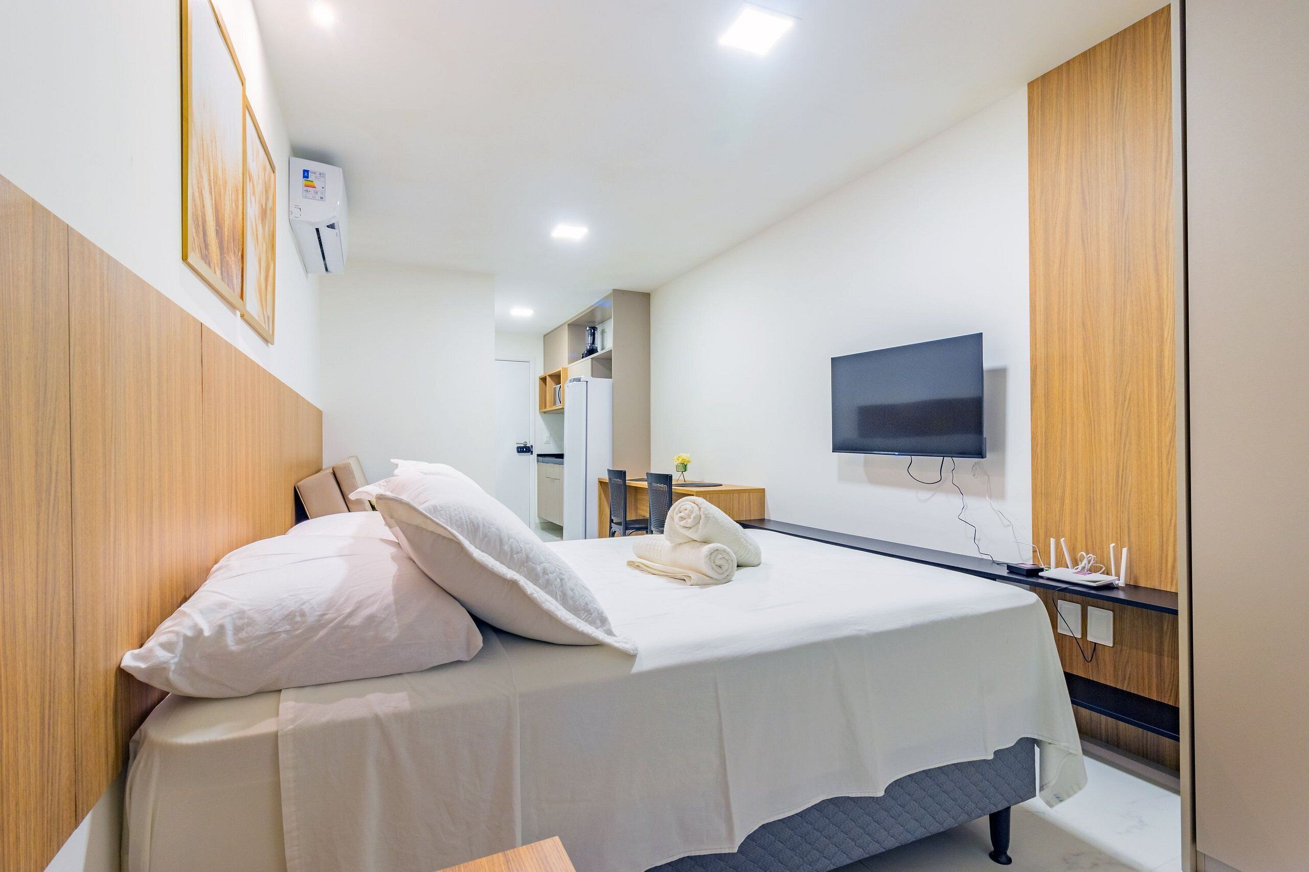 Ein Hotelzimmer mit Bett, Wandfernseher und Schreibtisch mit Computer und Telefon.