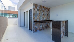 A modern outdoor kitchen area with a patterned backsplash, a built-in bar counter, and a sliding glass door leading to a balcony. - Porto City #314 - Porto de Galinhas by Carpediem (Ipojuca)