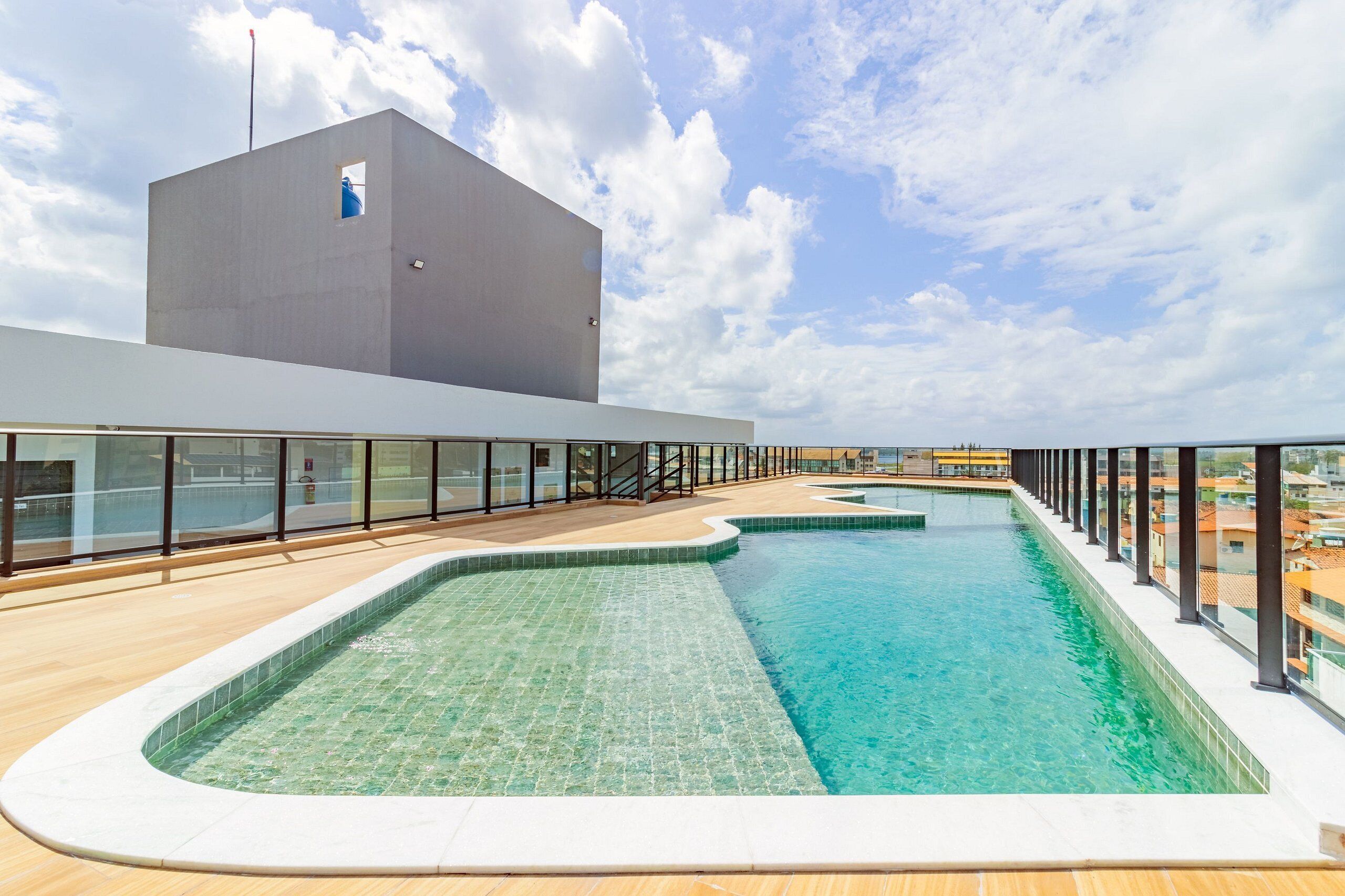 A rooftop swimming pool with clear blue water, surrounded by a wooden deck and glass railings.