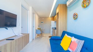 Ein modernes Wohnzimmer mit einem blauen Sofa, einem flachbildfernseher an einer Holzkonsole und einer kleinen Essecke mit Tisch und Stühlen.