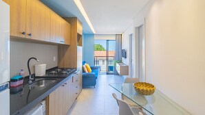 Eine moderne Küche mit schwarzem Arbeitsplatz, einem Herd und einem Spülbecken. Im Wohnbereich befindet sich eine blaue Couch und ein Glastisch mit Stühlen.
