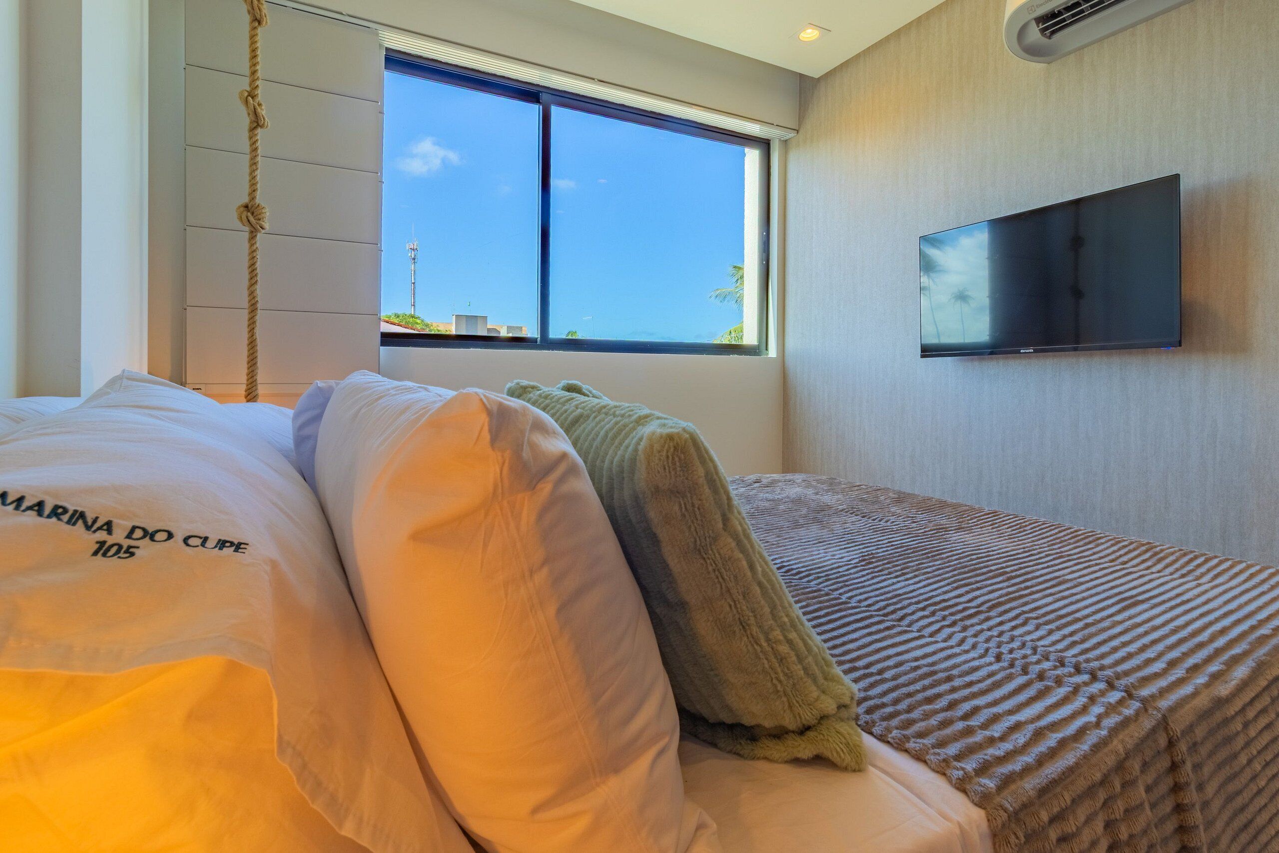 Ein Schlafzimmer mit Bett, einem Fenster mit Ausblick, einem Flachbildfernseher an der Wand und einer Kordel an der Decke.