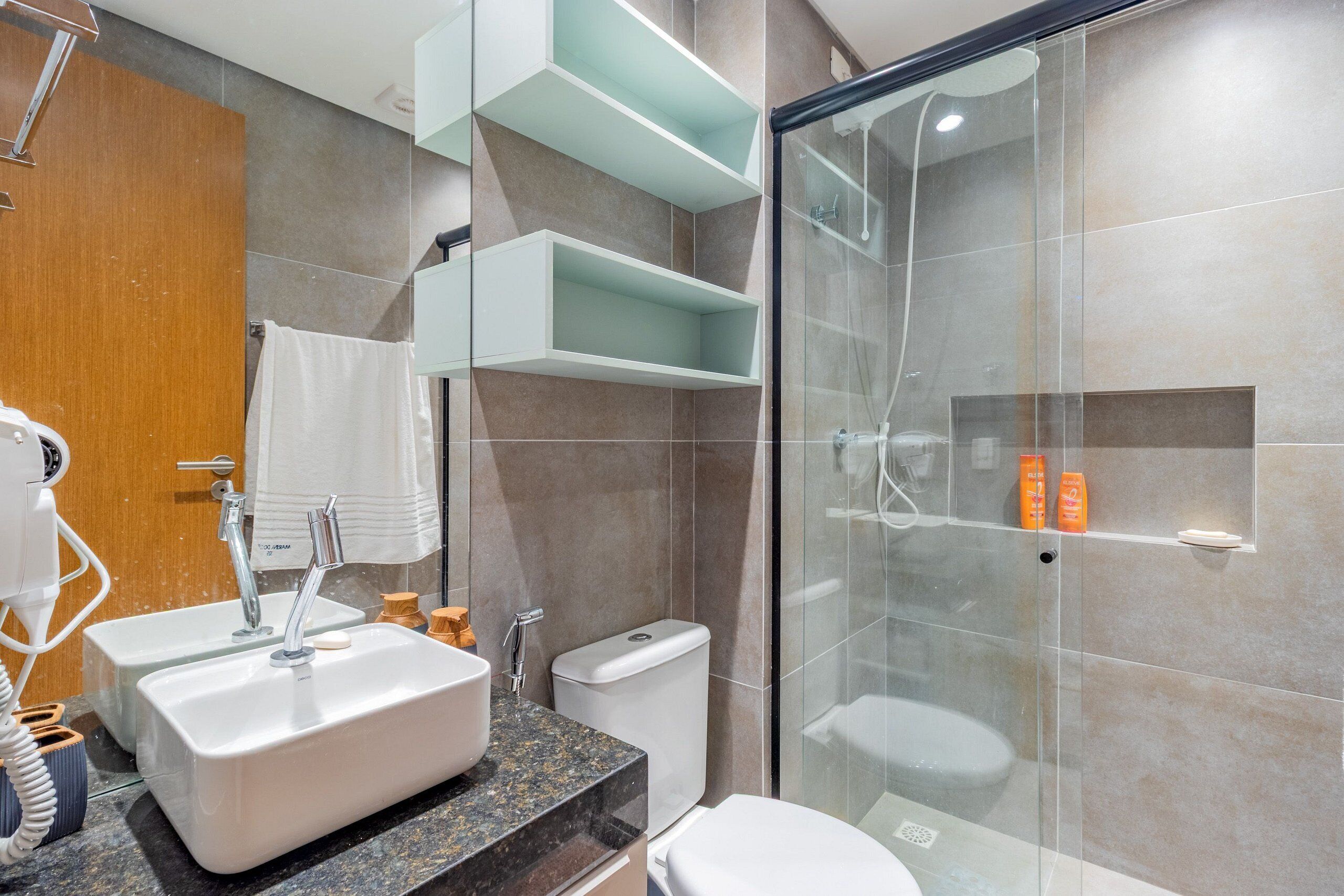 Un baño moderno con ducha envuelta en vidrio, un lavamanos blanco y un inodoro.