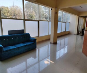 A spacious room with large windows, a blue sofa, and a tiled floor. - Hotel O RTO Office Krishnarajapura (Bengaluru)