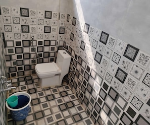 A bathroom with a toilet, a blue bucket, and patterned tiles on the walls and floor. - Hotel O RTO Office Krishnarajapura (Bengaluru)