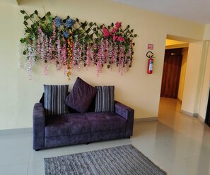A purple sofa with striped pillows, a patterned rug, and a wall-mounted floral arrangement. - Hotel O RTO Office Krishnarajapura (Bengaluru)