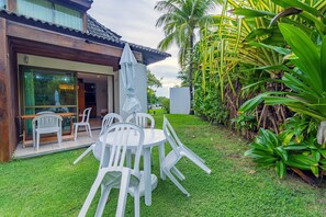 A patio with a white table and chairs, a glass door entrance, and lush greenery. - Beach Class #7113- Bungalow by Carpediem (Ipojuca)
