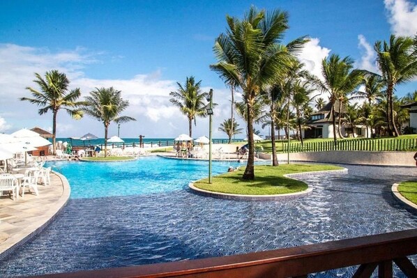 A resort pool area with palm trees, lounge chairs, and a view of the ocean. - Beach Class #7113- Bungalow by Carpediem (Ipojuca)