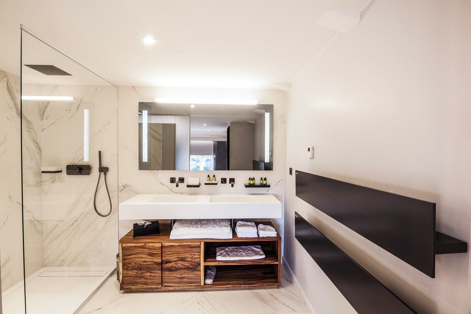 Een moderne badkamer met een grote spiegel, twee wasbakken, een douche en een houten wastafelmeubel met handdoeken.