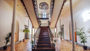 A grand staircase in a hotel lobby with a checkered floor, large columns, and potted plants. - Chateau de Roquefoulet (Montgeard)