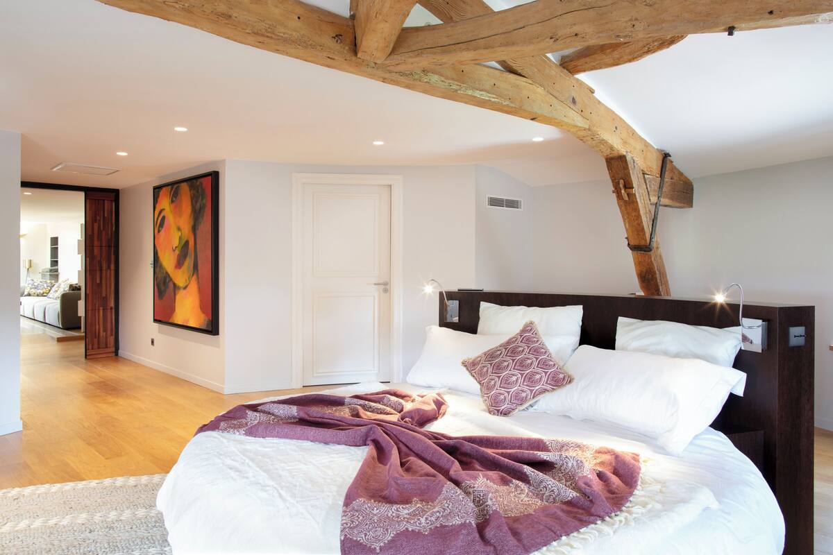 Une chambre avec un plafond en bois, un grand lit avec des oreillers blancs et à motifs, et un tableau accroché au mur.