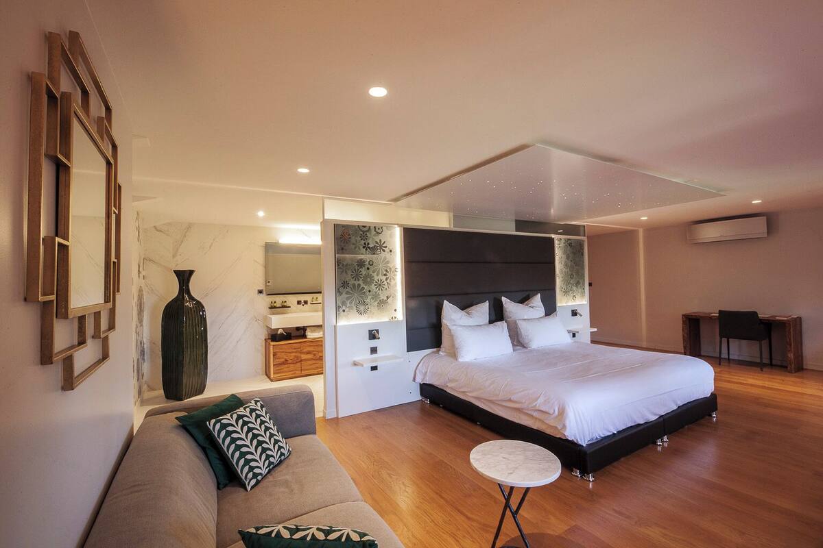 Une chambre moderne avec un grand lit, un canapé, une petite table ronde et une coiffeuse avec un miroir.
